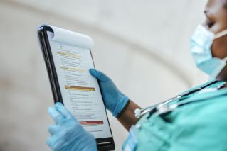 Side view of crop African American female medic in uniform reading text on paper at work